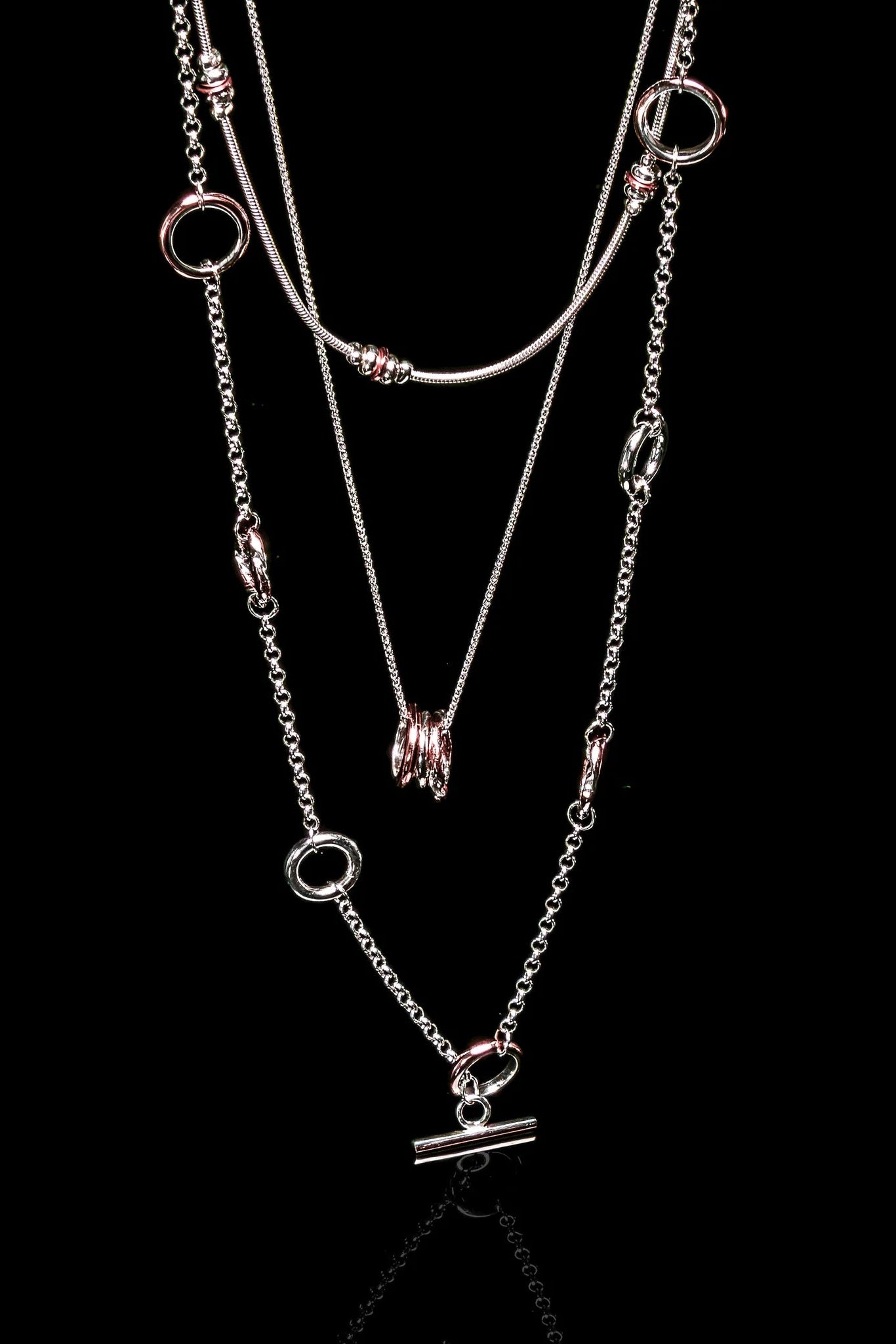 The Claudine Moncion Stack14 necklace is layered with other necklaces on a black background.