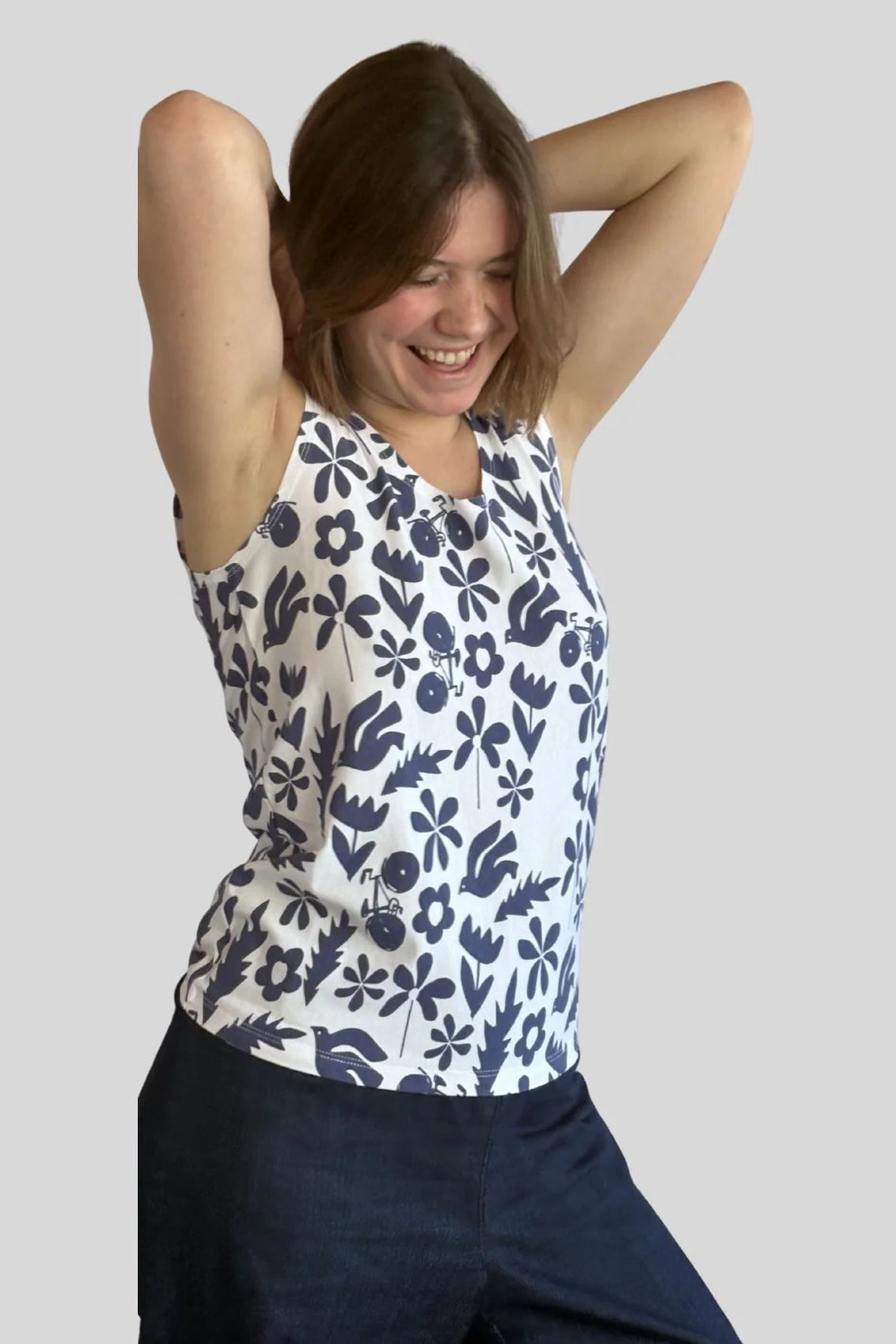 A woman wearing the Mimosa Tank Top by Message Factory, a sleeveless top in a blue floral print. She is wearing it with Navy pants and standing in front of a plain background.