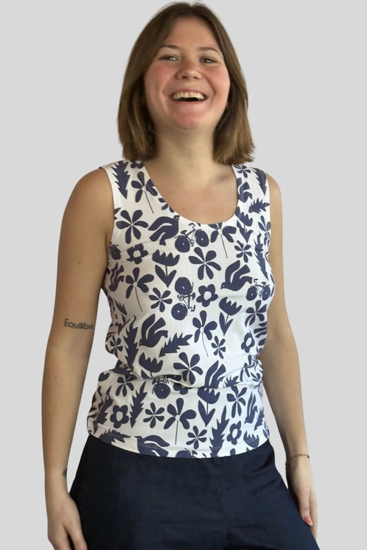 A woman wearing the Mimosa Tank Top by Message Factory, a sleeveless top in a blue floral print. She is wearing it with Navy pants and standing in front of a plain background.
