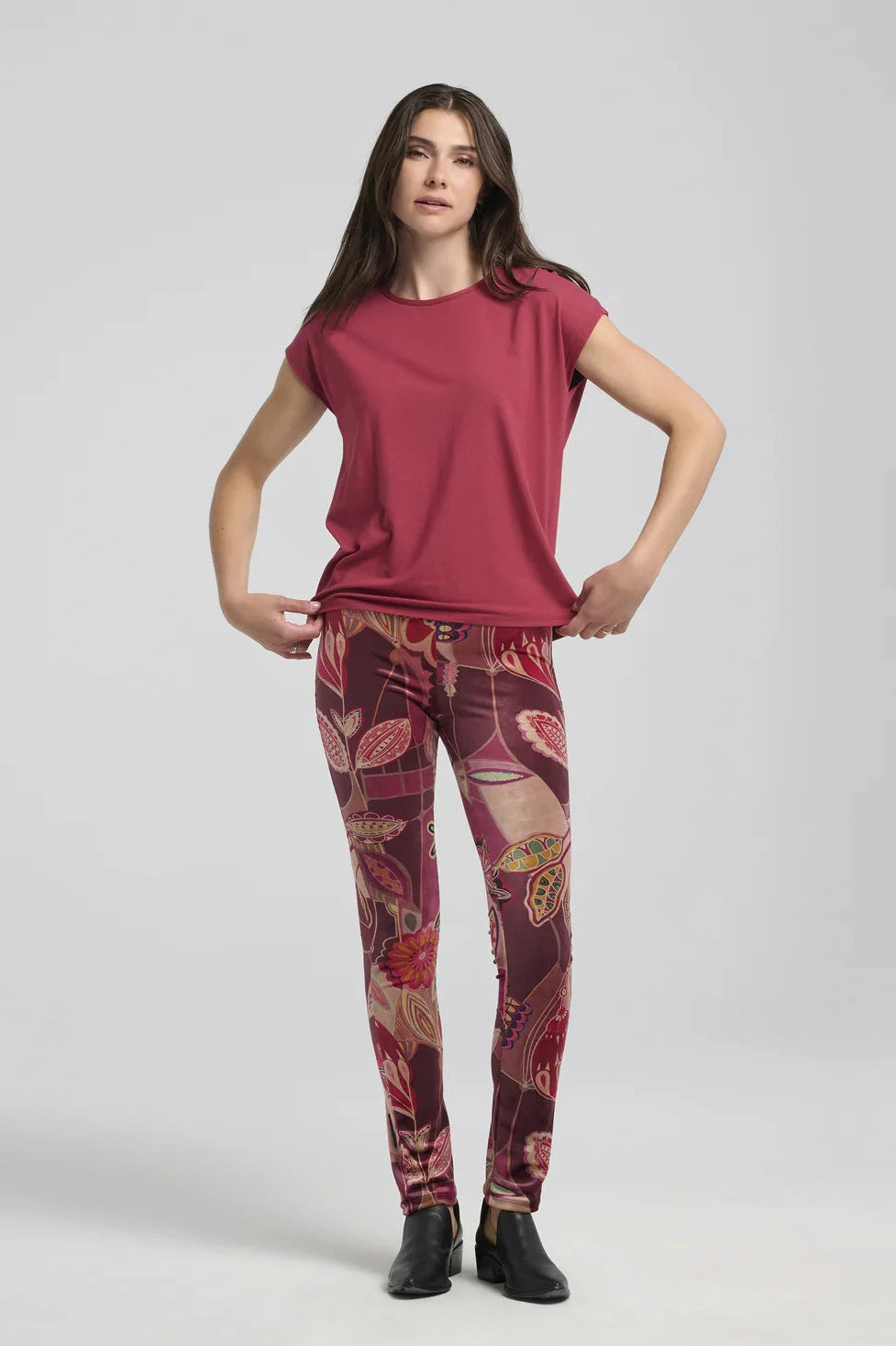 A woman wearing the Eowyn T-Shirt by Kollontai in Raspberry with patterned leggings standing against a grey background. 