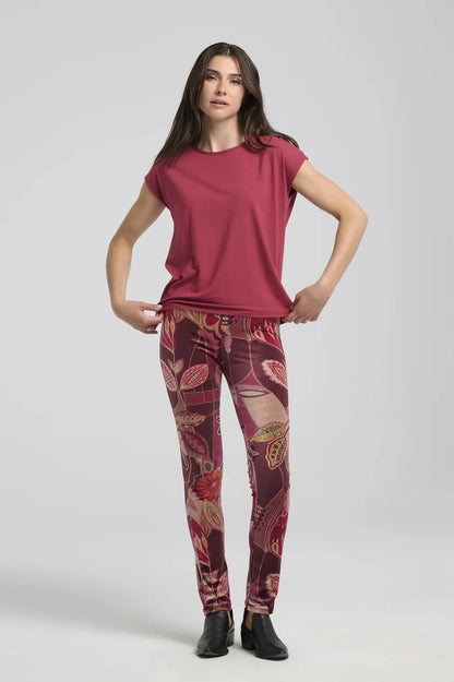 A woman wearing the Eowyn T-Shirt by Kollontai in Raspberry with patterned leggings standing against a grey background. 
