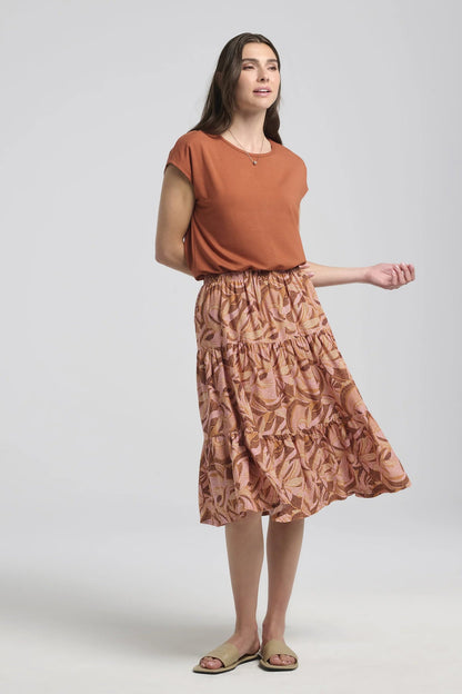 A woman wearing the Al-Uzza Skirt by Kollontai in Cinnamon print, a tiered skirt with an elastic waist and a below-the-knee length, with the Eowyn top in Rust. She is standing in front of a white background.