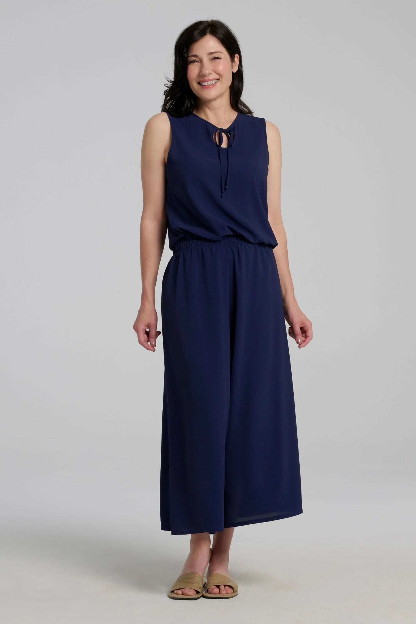 Woman wearing the Ishara Pants by Kollontai, cropped palazzo pants with ultra-wide legs and an elastic waistband. She's wearing them with a navy sleeveless top and standing in front of a grey background. 