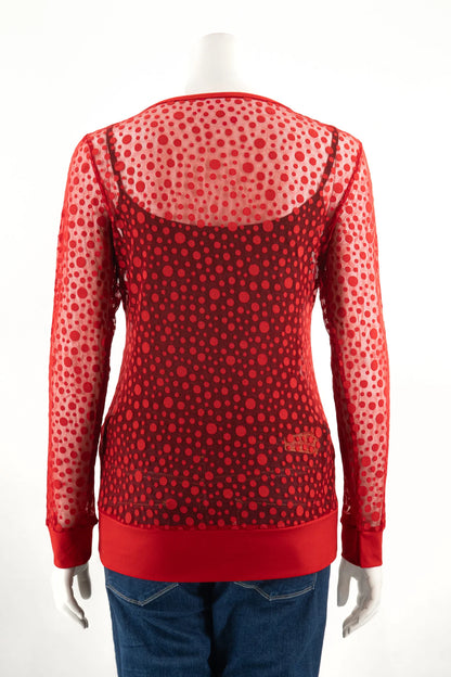 A back view of the Daisy Lace Top by Karkass in Grenade in shown on a mannequin with jeans against a white background. It's a long sleeved shirt with a round neck in sheer red mesh with a polka dot pattern.