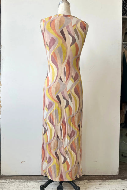 A back view of the Serina Dress by Kollontai in Peach print, a long, slim cut sleeveless dress with a soft pleat at the waist, is shown on a mannequin in front of a white background. 