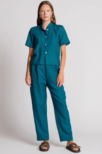 A woman wearing the Sparrow pants by Allison Wonderland in Ocean, straight-ish pants with an elastic waist. She is wearing them with the matching Kite Top  and standing in front of a plain background. 