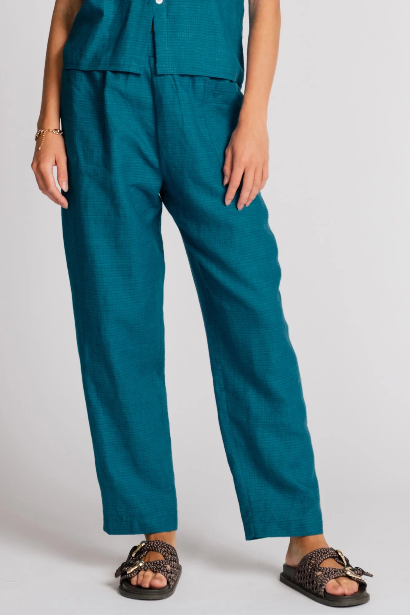 Waist-down view of a woman wearing the Sparrow pants by Allison Wonderland in Ocean, straight-ish pants with an elastic waist. She is wearing them with the matching Kite Top and standing in front of a plain background. 