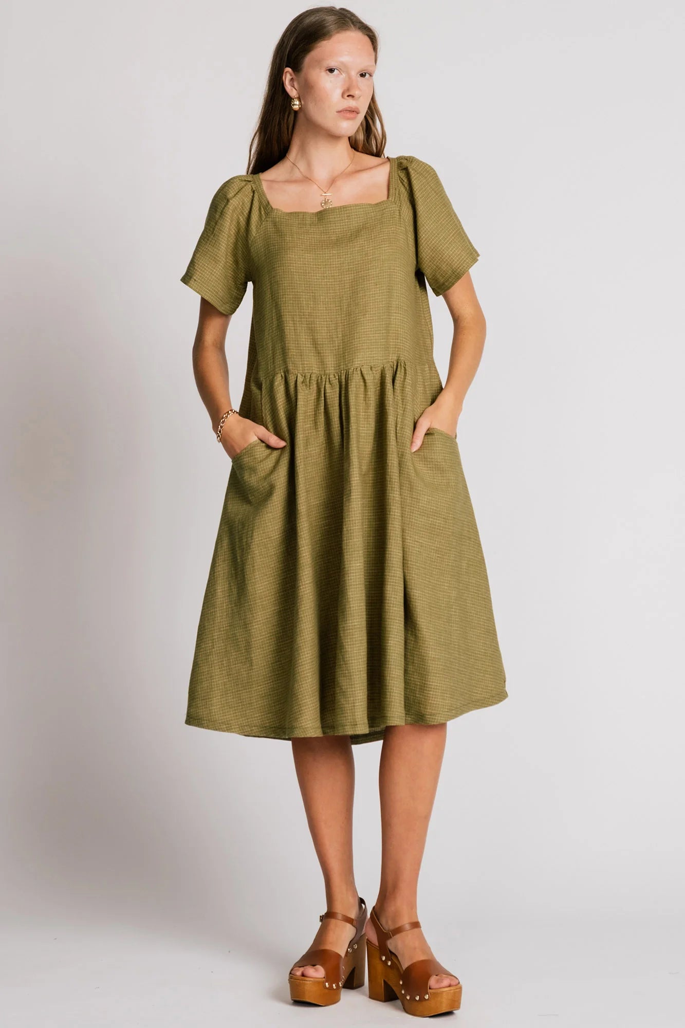 Woman wearing the Warbler Dress by Allison Wonderland in Avocado, a mid-calf length dress with short puffed sleeves and a square neckline. She is standing in front of a plain background. 
