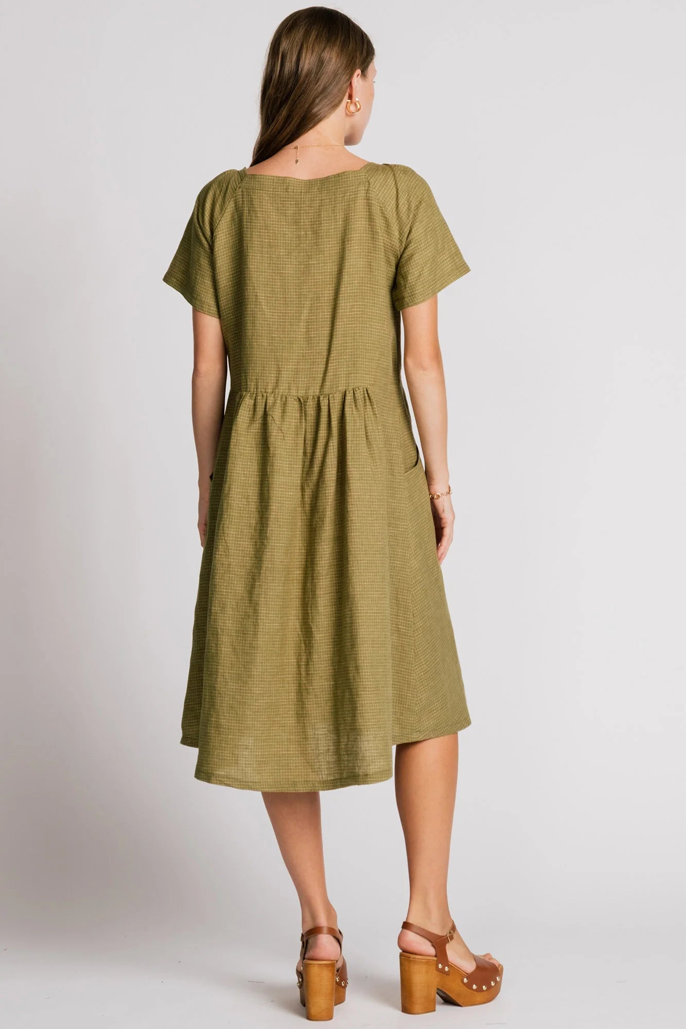 Back view of a woman wearing the Warbler Dress by Allison Wonderland in Ocean, a mid-calf length dress with short puffed sleeves and a square neckline. She is standing in front of a plain background. 