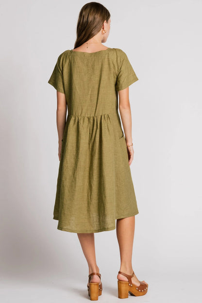 Back view of a woman wearing the Warbler Dress by Allison Wonderland in Ocean, a mid-calf length dress with short puffed sleeves and a square neckline. She is standing in front of a plain background. 