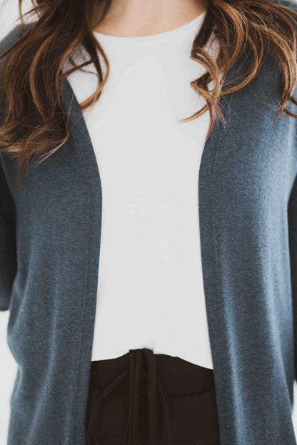 Close up detail of a woman wearing the Carolina Duster Cardigan by Ang Hill in Juniper, a long open cardigan with long sleeves. She is wearing it with black pants and a white top.