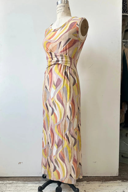 The Serina Dress by Kollontai in Peach print, a long, slim cut sleeveless dress with a soft pleat at the waist, is shown on a mannequin in front of a white background. 