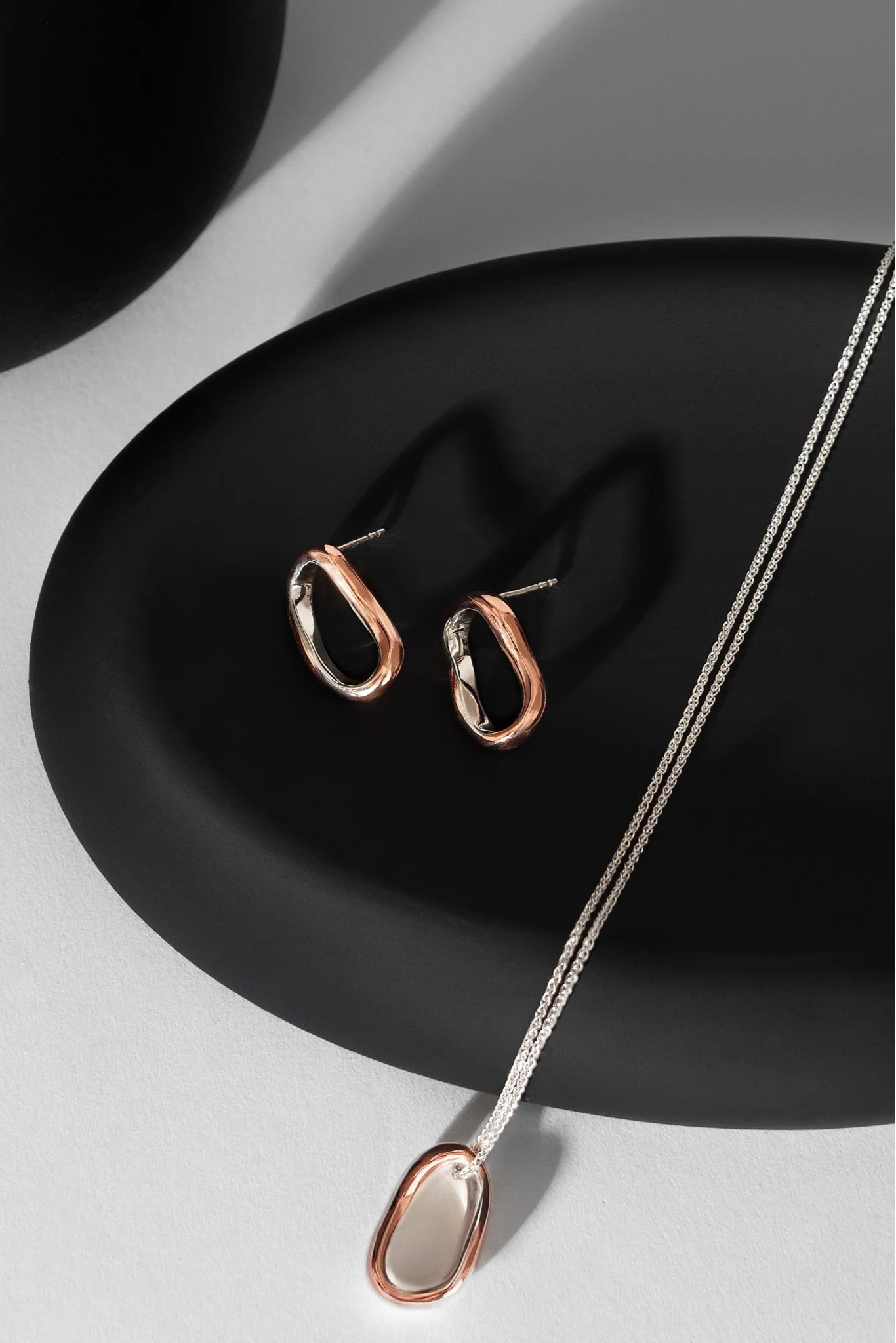 Copper and silver hoop earrings and necklace on a black plate with a white background