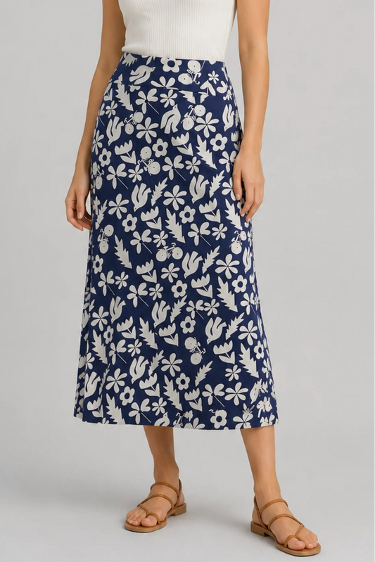 Waist down view of a woman wearing the Chertsey Skirt by Message Factory in blue and white Summer Print, a midi-length A-line skirt with a wide pull-on waistband. She is wearing it with a white top and standing in front of a white background. 