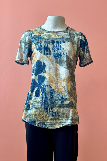 The Gladys T-shirt by Pure Essence in Golden Multi print is shown on a mannequin against a coral background. 