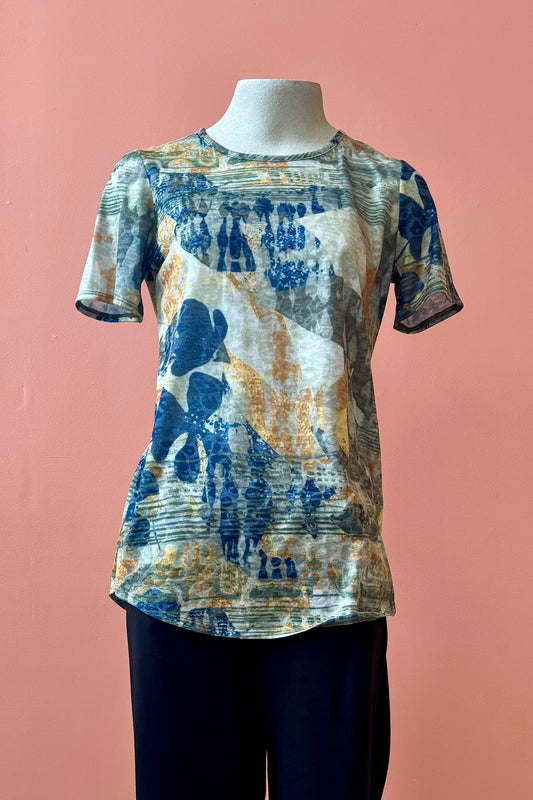 The Gladys T-shirt by Pure Essence in Golden Multi print is shown on a mannequin against a coral background. 