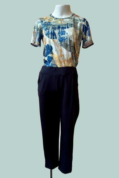 The Giselle Joggers by Pure Essence in Black are shown on a mannequin with a patterned shirt in front of a turquoise background. 