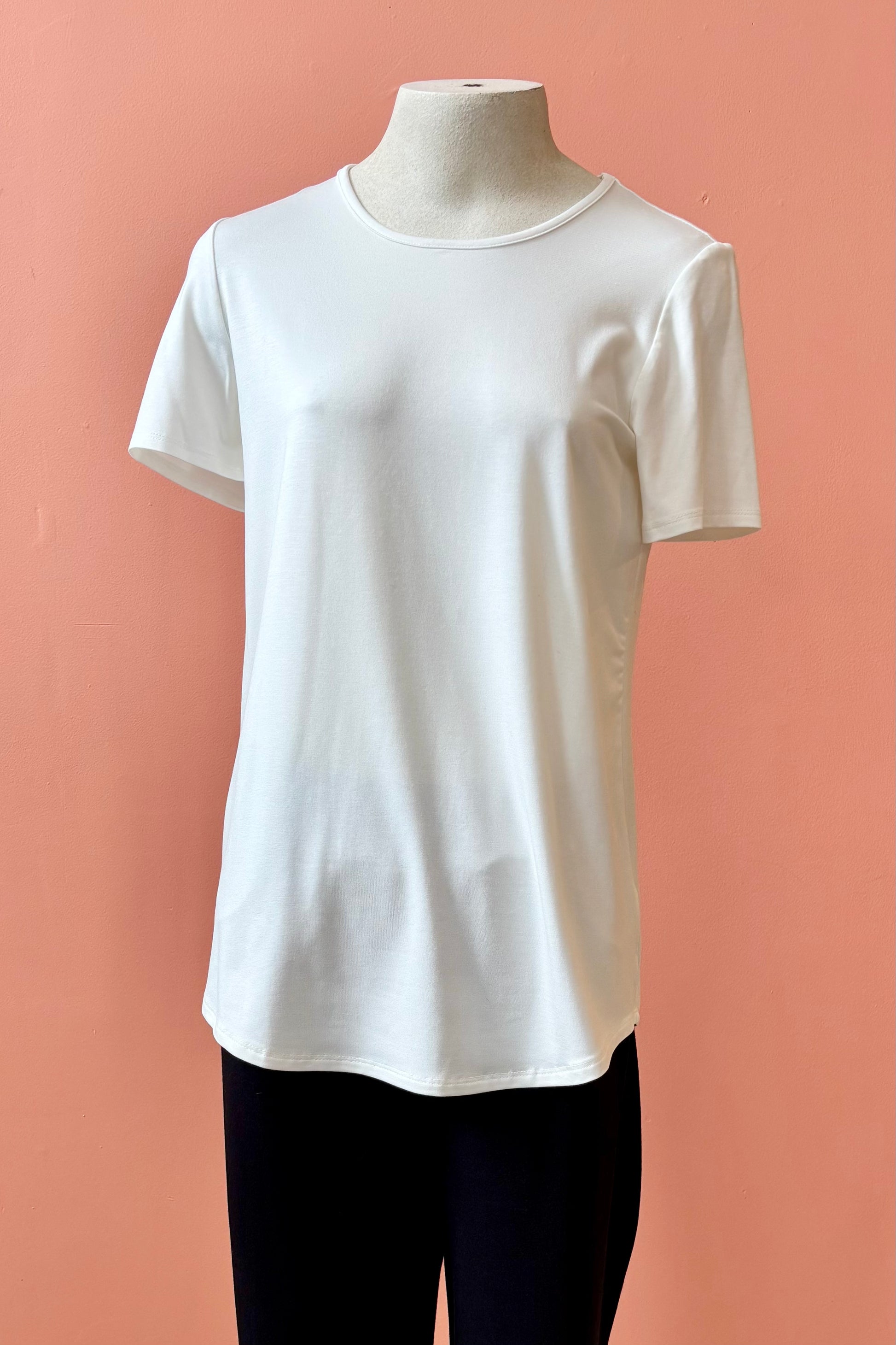 The Gladys T-shirt by Pure Essence in White is shown on a mannequin against a coral background. 
