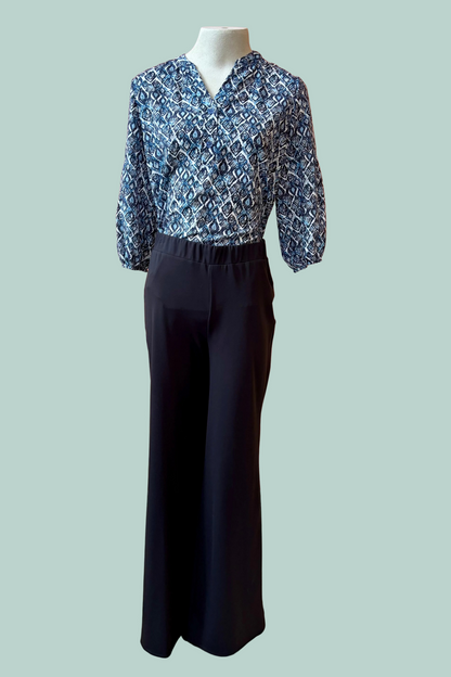 A mannequin wearing a the Gloria Pants by Pure Essence in Black with a blue patterned top on a light teal background