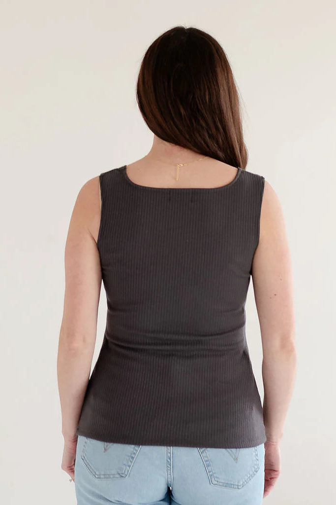 Back view of a woman wearing the Ang Hill Tracey Tank in Charcoal with wide straps, ribbed fabric, and a square neckline. She is wearing it with jeans and standing in a white room. 