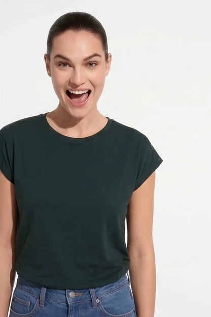 A woman wearing the Eowyn T-Shirt by Kollontai in Green with jeans standing against a grey background. 