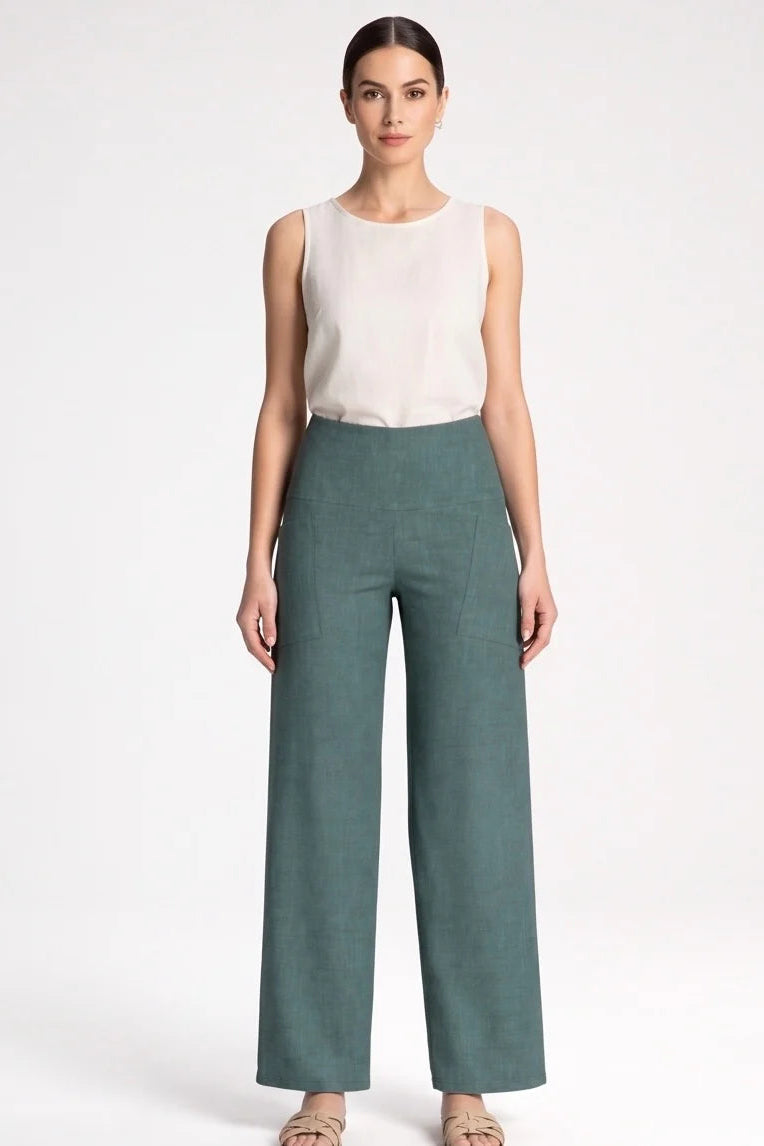 A woman wearing the Kollontai Susan Pants in Green with a white tank, standing in front of a grey background. 