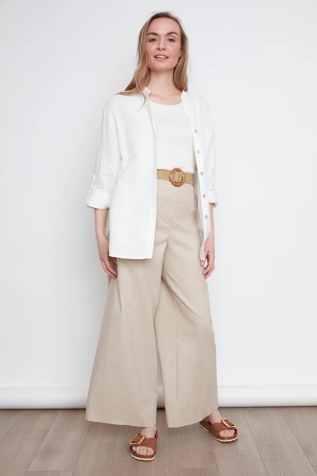 A woman wearing the jasmine Long Sleeve Shirt by Julei in Natural White, a classic dress shirt style with a mandarin collar, pleated pocket, and cuffed sleeves. She is wearing it with jeans and standing in front of white background. 