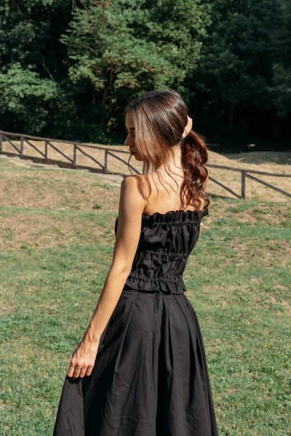 Back view of a woman wearing the Savannah maxi skirt from MAS in black and a ruched black tube top, standing outdoors.