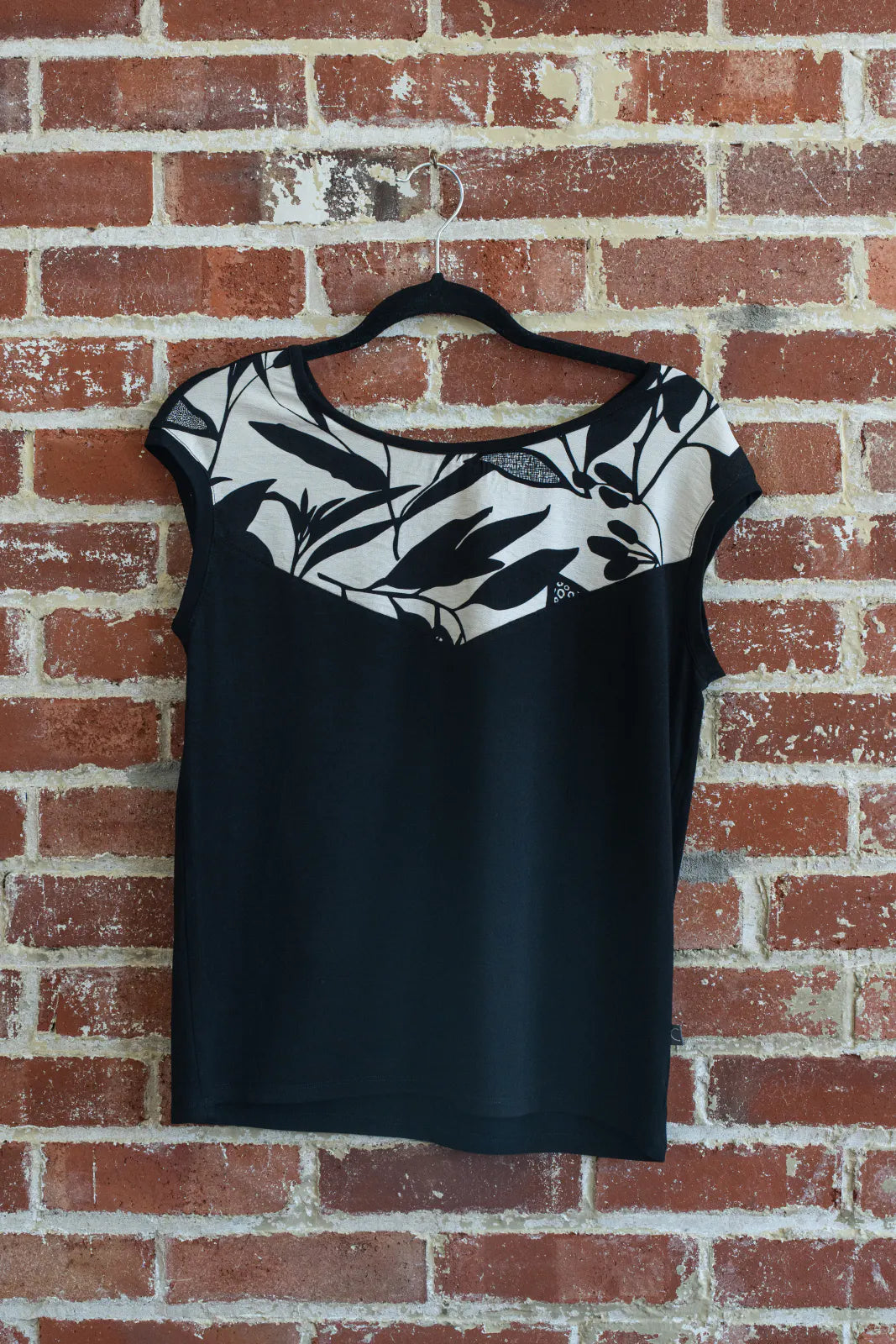 The Pepita Top from Marie C, a reversible t-shirt with a printed fabric yoke on one side, in Black and White is shown hanging on a brick wall.