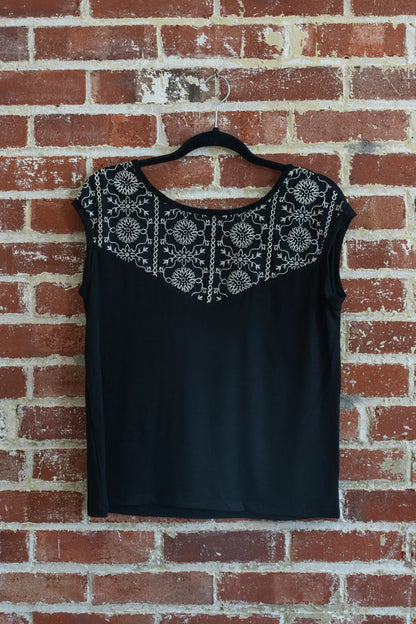 The Pepita Top from Marie C, a reversible t-shirt with a printed fabric yoke on one side, in Black with Print, is shown hanging on a brick wall.
