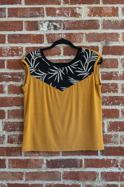 The Pepita Top from Marie C, a reversible t-shirt with a printed fabric yoke on one side, in Yellow, is shown hanging on a brick wall.