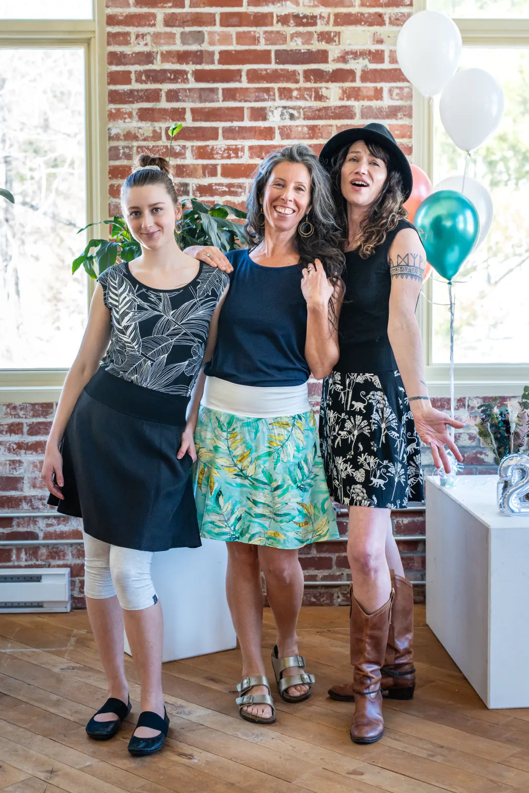 Three women wearing the Sol Top from Marie C, a reversible cap sleeve tee. From left to right they are wearing it in Black with Print, Navy, and Black. They are all wearing skirts and are standing at a party. 