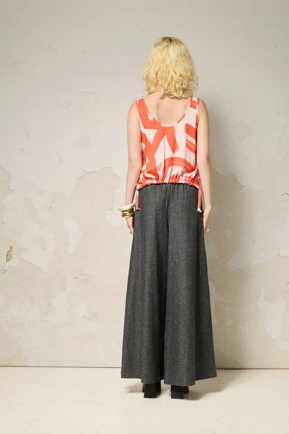 Back view of a woman wearing the Osiris Tank Top by Cokluch in Red Shodo print, with wide straps, a round neck, and a drawstring at the hem that can be worn at the front or back. She is wearing it with denim pants and standing in front of a grey background. 