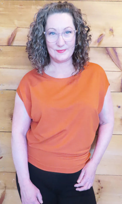 A woman wearing the Charles Slouch Tee by Mandala in Russet, standing in front of a wood panelled wall 