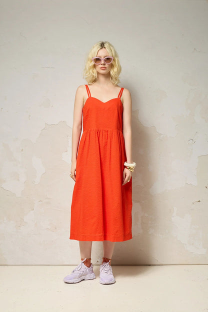  A woman wearing the Thalassa Dress by Cokluch in Fiesta, a midi dress with double spaghetti straps, a sweetheart neckline, and elastic smocking at the back, all in waffle textured cotton. She is standing against a plain background