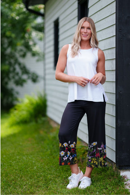 A woman wearing the Amaretto 7/8 Gaucho Pants from Rien ne se Perd in Black with a floral print hem. She is wearing them with a white top and standing outside.