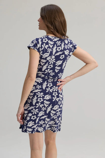 Back view of a woman wearing the Libellule Dress by Message Factory in Blue Print, a short sleeved wrap dress that falls to the knee. She is standing against a plain background. 