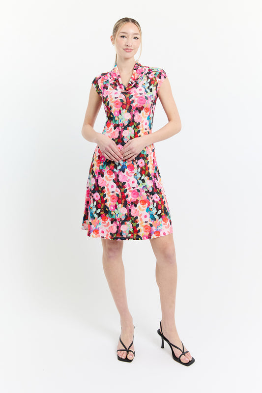 A woman wearing the Sky Dress by Dinh Ba in Pink print, an A-line floral dress with a cowl neck, cap sleeves, and above the knee hem. She is standing in front of a white background. 