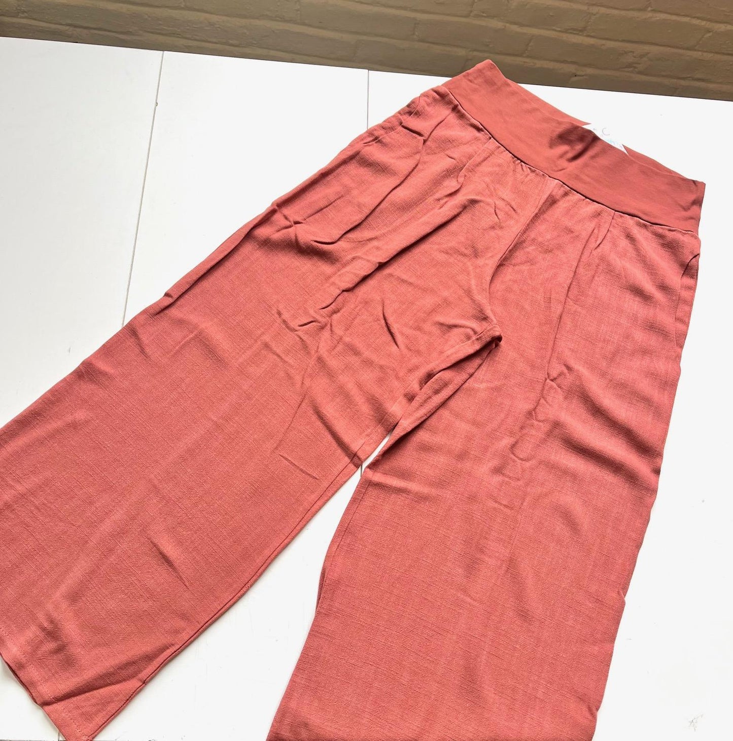 The Verano Pants by Marie C in Coral are shown laid flat on a white table. 
