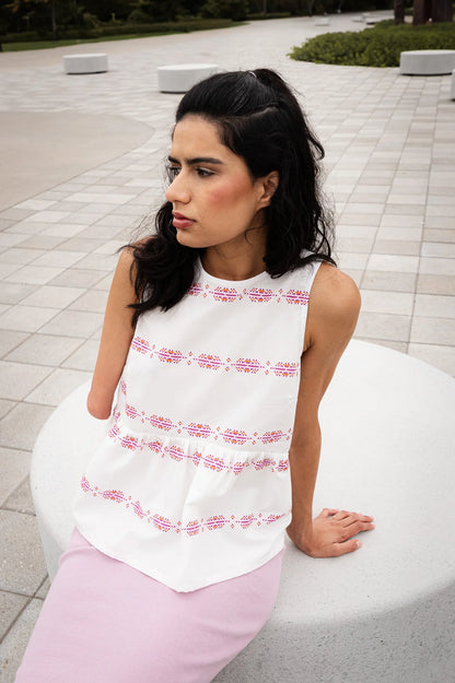 Back view of a woman wearing the Malé Top from MAS, a sleeveless top with a peplum and ties up the back. She is wearing it with wide-leg pants and sitting outdoors on a paved pathway.
