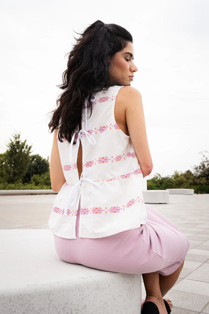 Back view of a woman wearing the Malé Top from MAS, a sleeveless top with a peplum and ties up the back. She is wearing it with wide-leg pants and sitting outdoors. 