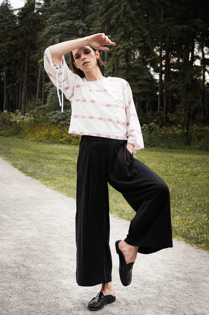 A woman wearing the Siena Pants by MAS in Pepper, wide legged trousers with an elastic waist. She is wearing them with a white top and standing outdoors. 