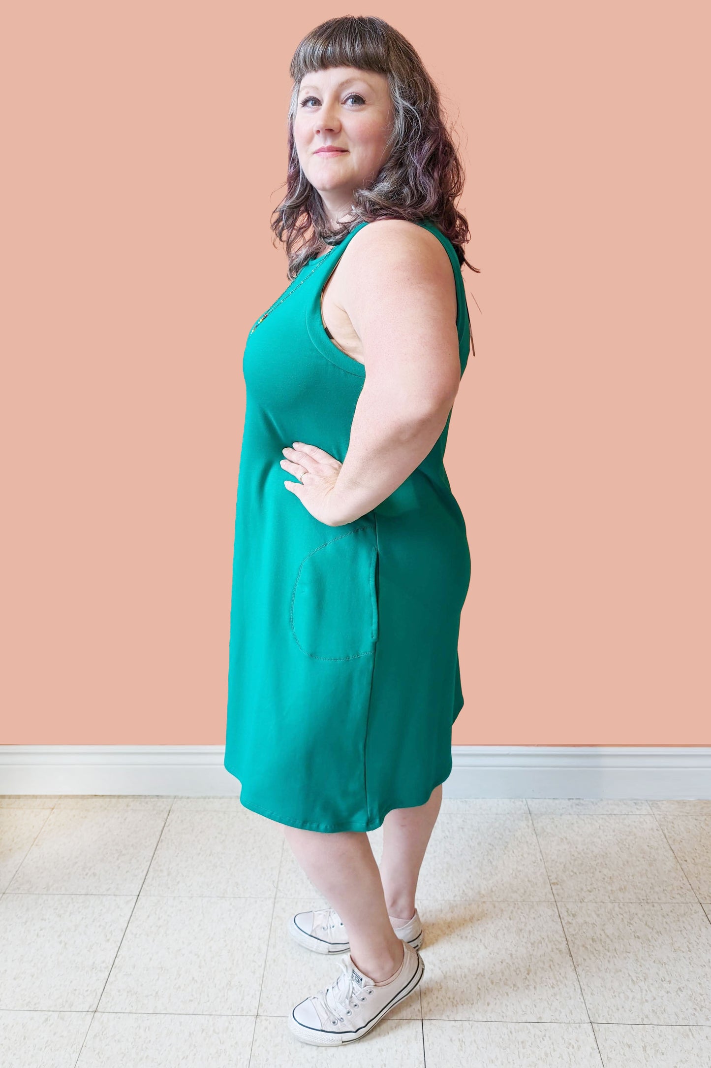 Side view of Allana  wearing the Cheri Dress by Pure Essence in Kelly Green, standing in front of a coral wall