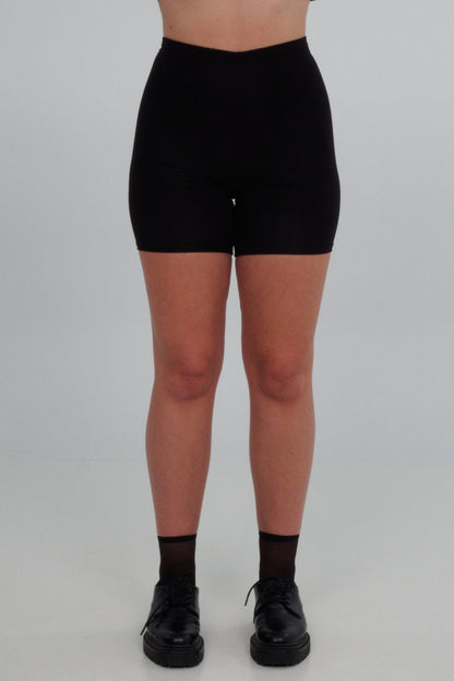 A woman wearing Slak's bike shorts in Black, with a very high waist and a soft modal knit. She is standing in front of a grey background. 
