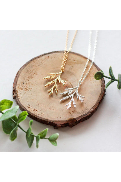 Juniper branch necklace by Birch Jewellery; shown in silver and hold; flat lay on a stump of would and with eucalyptus branches